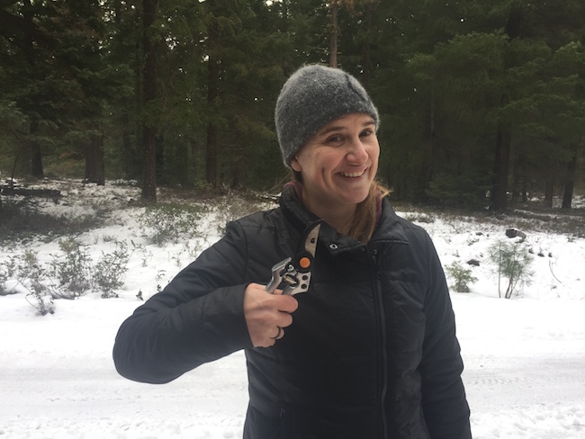 A smiling woman holding clippers in a jocular manner in the snow