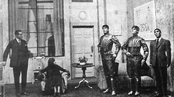 scene from play about robots, three robots on the right, man in a suit on the left