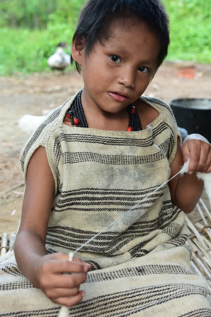 A girl of about seven with short black hair in a homespun garment, spinning cotton on a single spindle