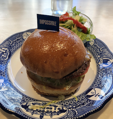 A burger on a blue plate with a small flag that reads "impossible" 