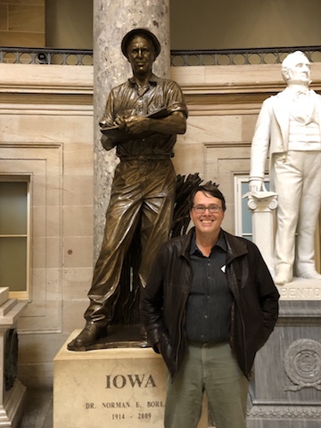 Charles Mann smiles in front of a statue of Norman Borlaug