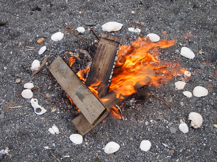 A small fire on the beach, ringed with white seashells