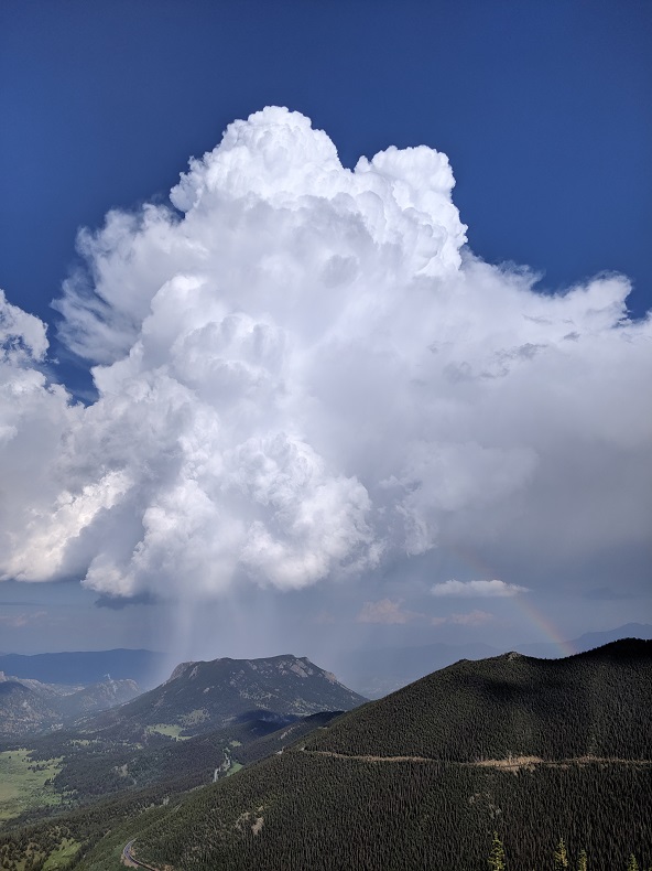 tall storm cloud over a green mountain, with a rainbow