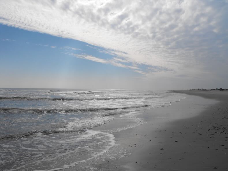 A peaceful beach below a blue sky and a frilly band of white cloud