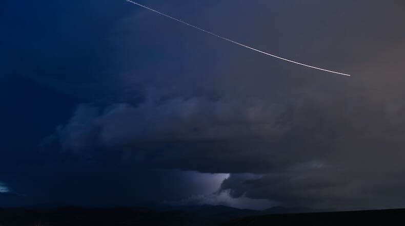 A falling star, or perhaps an airplane, streaks across an ominously dark sky