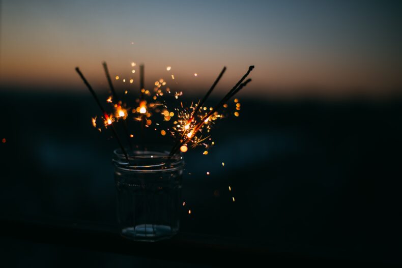 A glass jar filled with lit sparklers at sunset, the glittering sparks illuminating the dusk.